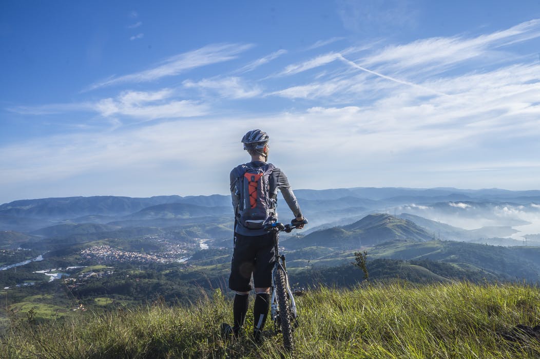 A man looking to the horizont in a sunny day from the top of a mountain with his bike